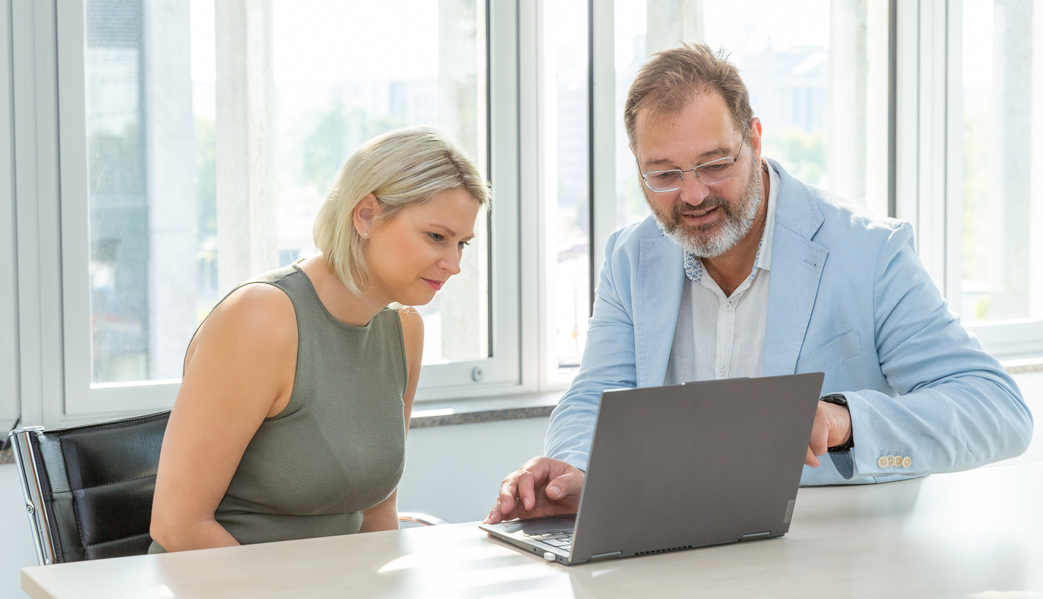Eine blonde Frau und ein Mann mit Bart lächeln und schauen gemeinsam auf einen Laptop